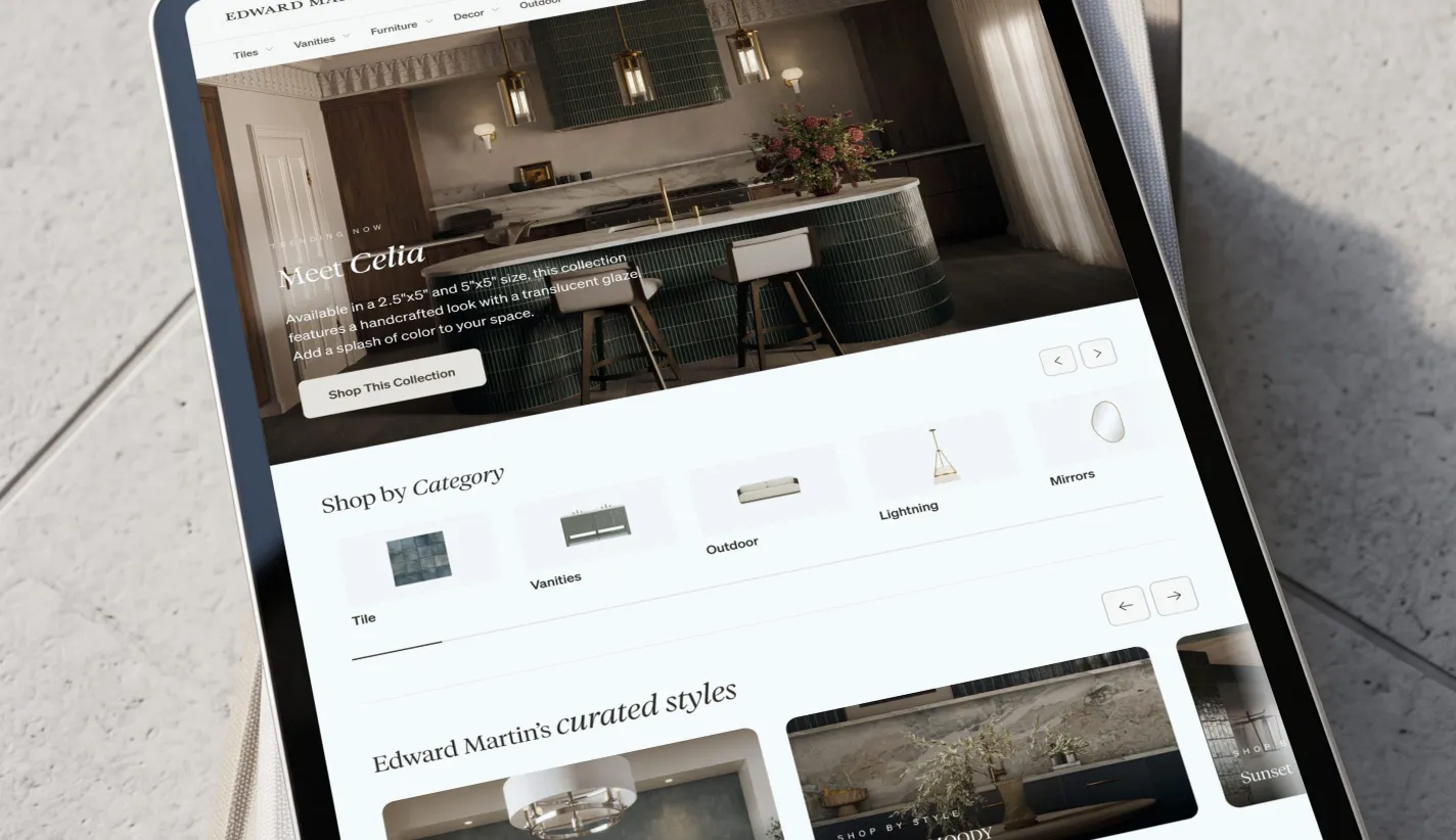 The Edward Martin home page on a tablet lying at an angle on pale concrete — a Meet Celia collection hero photographed in a green-tiled kitchen, a Shop by Category row of tile, vanity, outdoor, lighting and mirror tiles, and the start of Edward Martin's curated styles